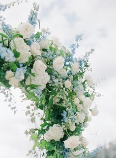 white and blue flowers are hanging from a pole with greenery in the foreground