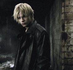 a young man with blonde hair wearing a black leather jacket standing in an alleyway