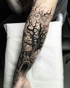 a man's arm with a tree and clouds tattoo on the left side of his arm