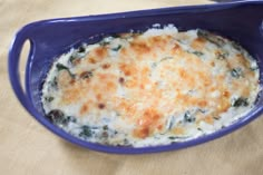 a casserole dish with cheese and spinach in a blue bowl on a table