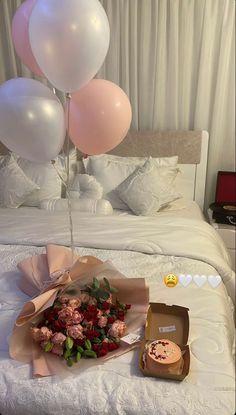 a bouquet of flowers and balloons on a bed with a box of donuts next to it