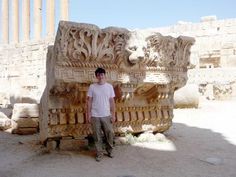 a man standing next to a stone sculpture in front of a building with columns on it