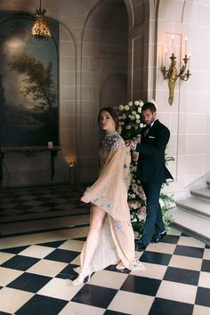 a woman in a dress standing on a checkered floor next to a man in a tuxedo