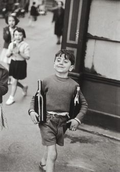 a little boy walking down the street with a bottle of wine in his hand and two other children behind him