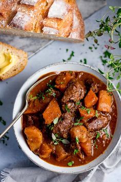 two hands holding a bowl of beef stew with bread and parsley on the side