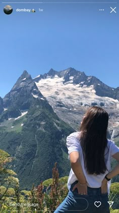 a woman standing on top of a lush green hillside next to a snow covered mountain