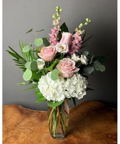 a vase filled with pink and white flowers on top of a wooden table next to a gray wall