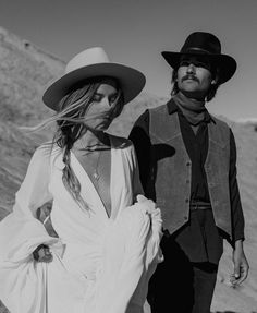 black and white photograph of man and woman in cowboy hats walking on the beach together