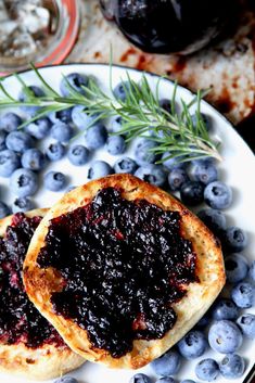 two blueberry pies on a white plate with fresh blueberries and rosemary sprigs