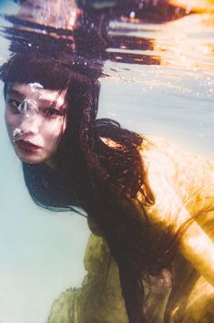 a woman in a yellow dress is under water with her hair blowing back and looking at the camera