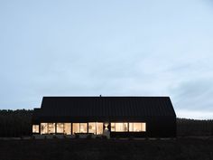 a black house is lit up at night in the country side with grass and trees