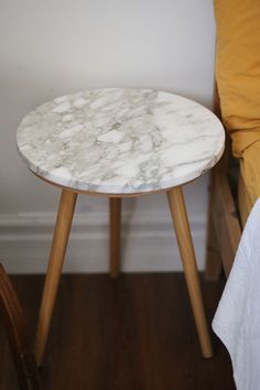 a white marble table sitting on top of a hard wood floor next to a bed