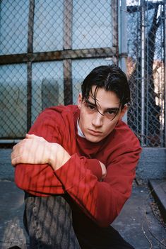 a young man leaning against a fence with his arms crossed