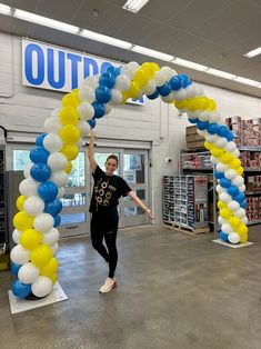 a woman is standing under an arch made out of balloons and streamers in a store