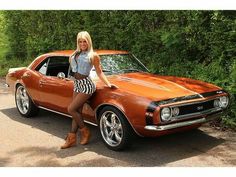 a woman standing next to an orange muscle car