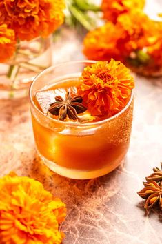 an orange flower in a glass filled with liquid and flowers on the table next to it