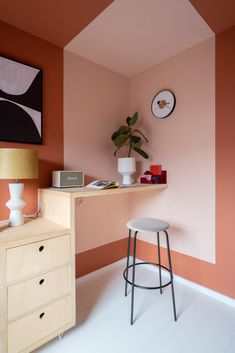 a room with pink walls and white flooring has a stool, table and lamp on it