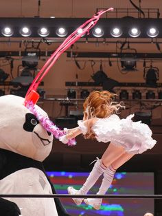 a woman in white dress standing next to a giant stuffed animal with pink ribbon on it's head