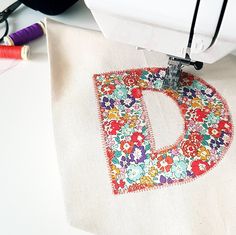 a sewing machine next to a piece of fabric with the letter d embroidered on it