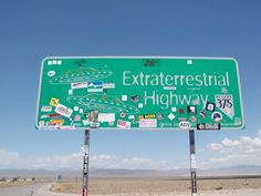 a green street sign sitting on the side of a road next to a dirt field