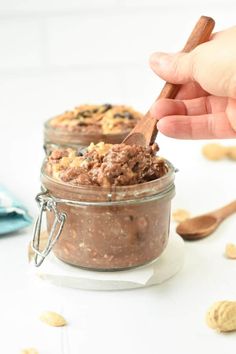 a hand holding a spoon over a jar filled with peanut butter and chocolate pudding