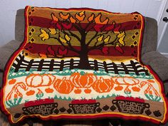 a blanket that is sitting on top of a chair in front of a wall with a tree and pumpkins