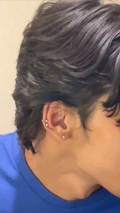 a close up of a person with black hair wearing ear piercings and a blue shirt