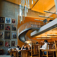 people are sitting at tables in a restaurant with spiral staircases and pictures on the wall