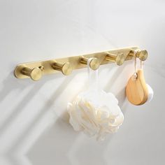 a gold coat rack with two wooden spoons hanging from it's hooks and a white flower