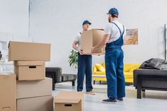 two men standing in a room with boxes on the floor and one holding a cardboard box