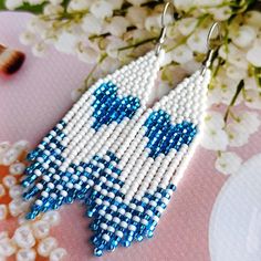 a pair of blue and white beaded earrings sitting on top of a pink table