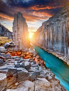 the sun is setting over an ancient canyon with blue water and large rock formations in the foreground