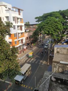 a city street filled with lots of traffic next to tall buildings and green trees on both sides