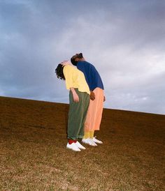 two people standing in the middle of a field with their arms around each other as if they are kissing