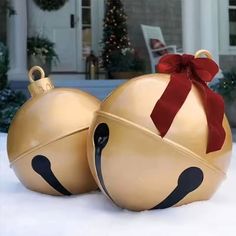 two gold christmas ornaments sitting in the snow with a red ribbon on top of them