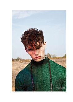 a young man with curly hair wearing a green shirt in the middle of a field