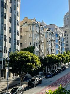 cars parked on the side of a street next to tall buildings and trees in front of them