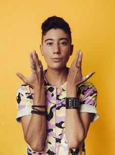 a young man with his hands in the air and wearing bracelets, standing against a yellow background