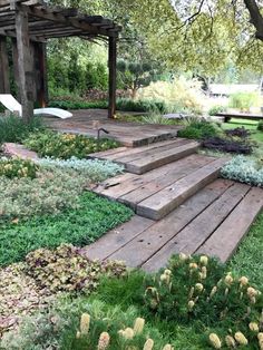 a wooden deck in the middle of a garden with flowers and plants growing on it