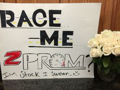 a sign that says race me 2 prom and white roses in a vase next to it