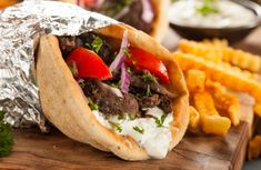 a taco filled with meat and vegetables on top of a cutting board next to fries