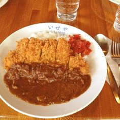 a white plate topped with meat covered in gravy next to rice and tomatoes