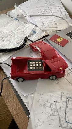 a red telephone sitting on top of a table next to papers and laptops with drawings