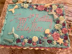 a blue birthday cake with pink and green decorations on the top that says happy at birthday ella mae