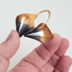 a hand holding a gold and black object in it's left hand, with the tip of its mouth open