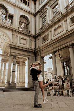 a man and woman standing in front of an old building with many books on the ground