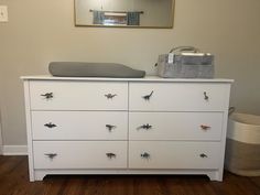 a white dresser with lots of bugs on it and a mirror hanging above the drawers