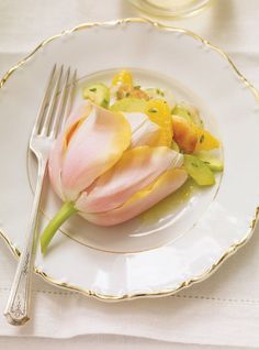 a white plate topped with a pink flower next to a fork