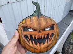 a hand holding up a carved pumpkin with teeth and fangs on it's face