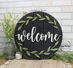 a welcome sign sitting on top of a wooden table next to a vase with flowers